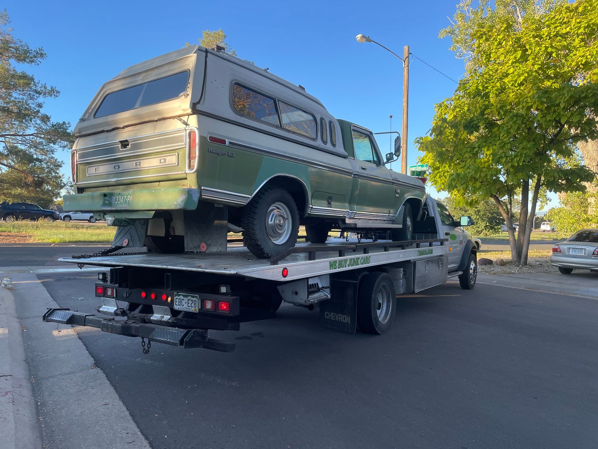 Green camper van strapped on a flatbed tow truck on a roadside near trees and streetlights.