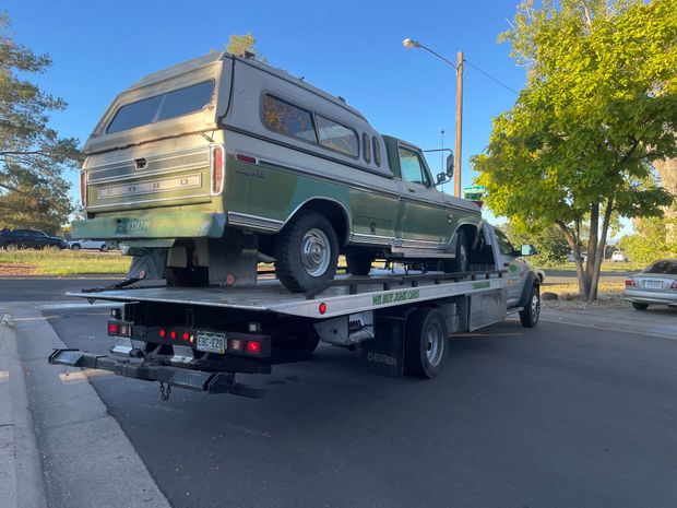 Green camper van strapped on a flatbed tow truck on a roadside near trees and streetlights.