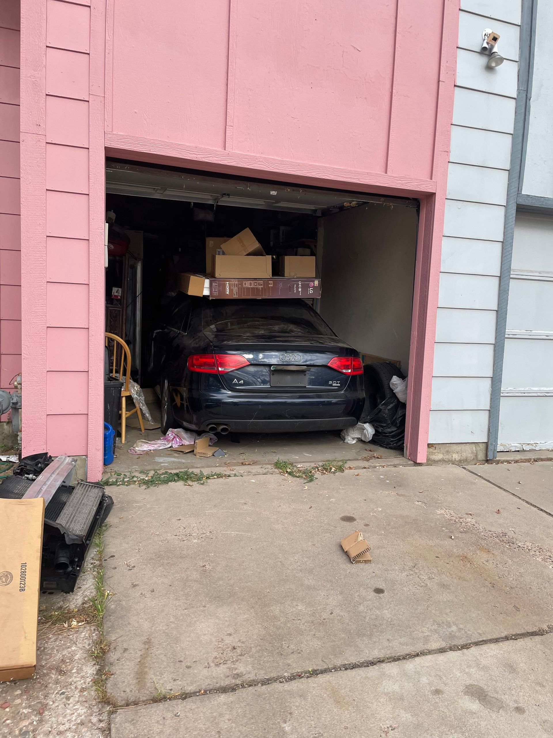 Black sedan parked in a partially open pink garage beside a concrete driveway