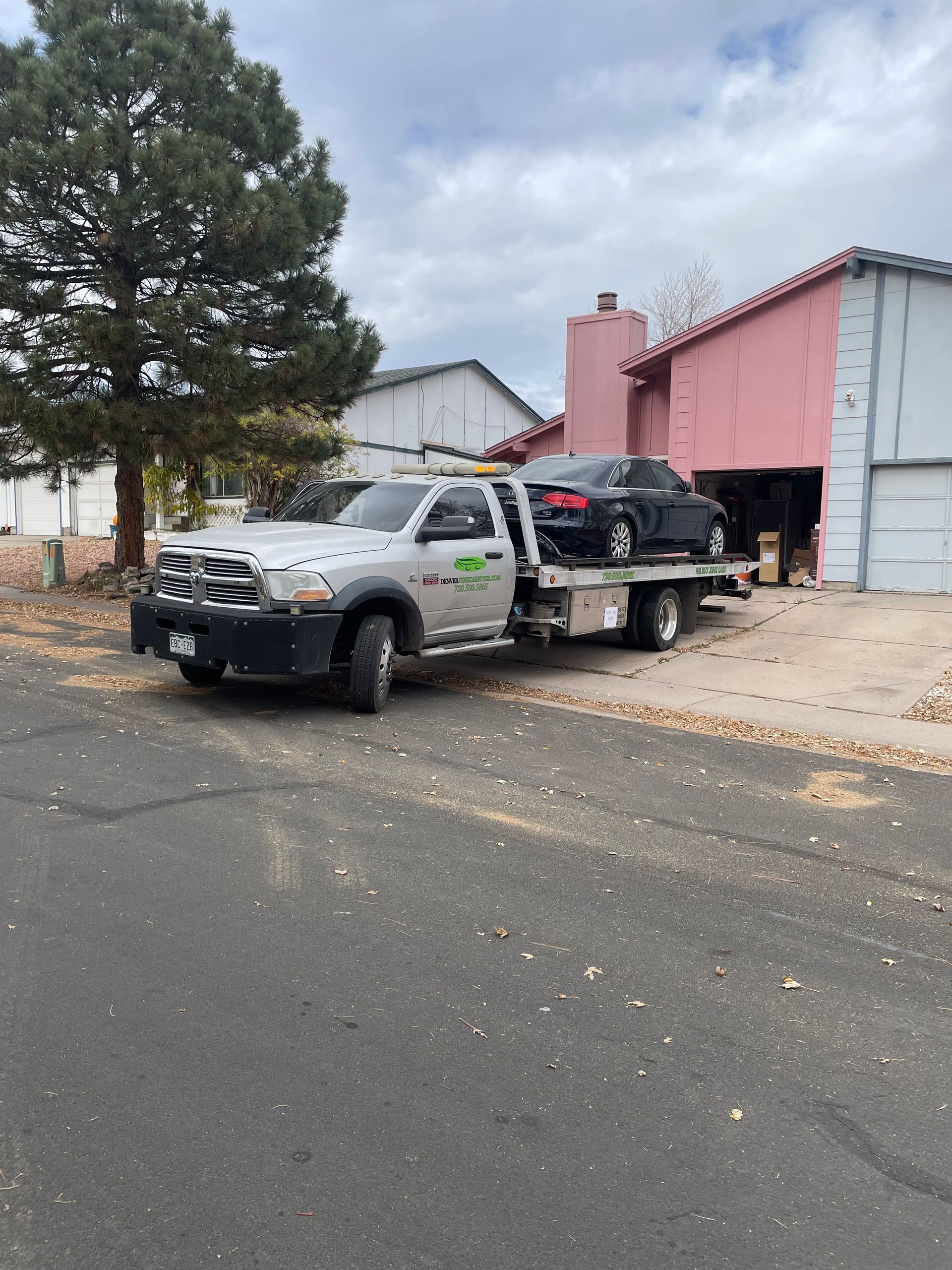 Tow truck hauling a black vehicle beside a pink building on a cloudy street