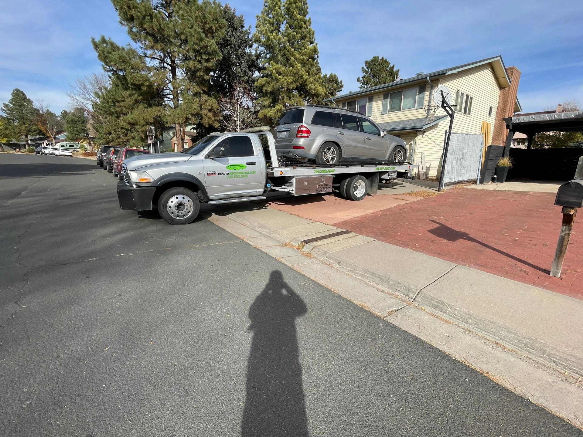 Pickup truck towing SUV up driveway beside a house; blue sky and curbside street.