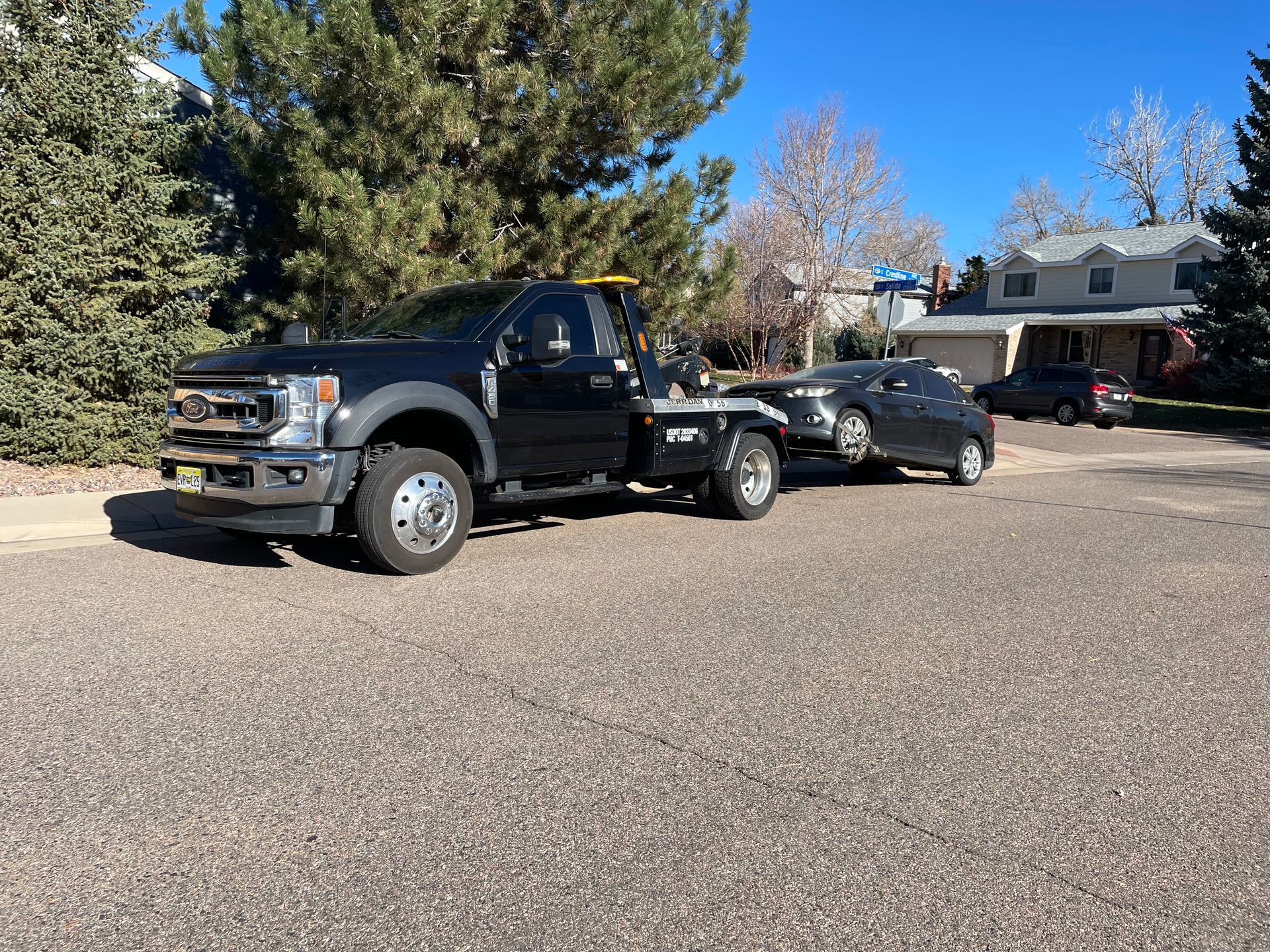 Black pickup truck towing a black coupe in a suburban driveway with trees and houses nearby