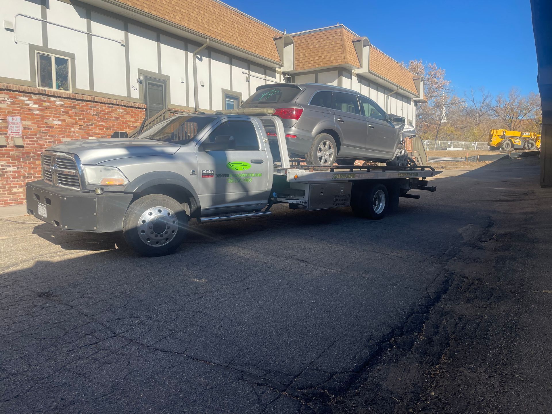 Gray SUV on a flatbed tow truck parked on a street beside buildings on a sunny day