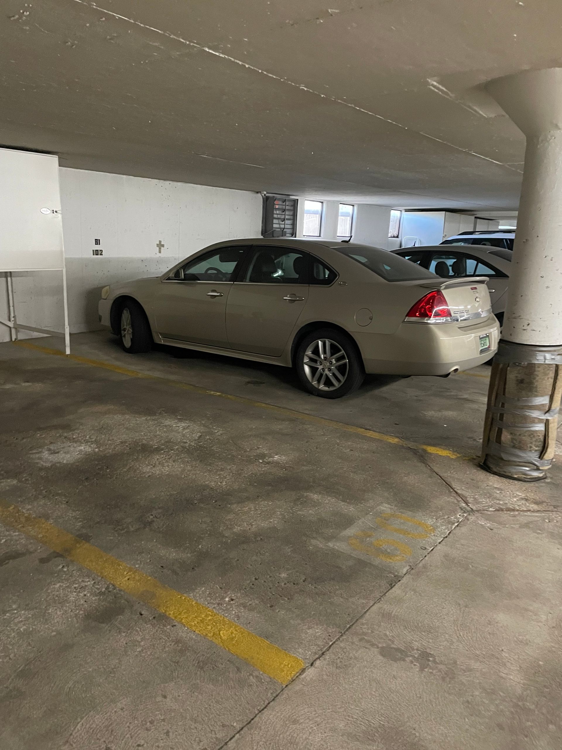 Beige sedan parked in a concrete parking garage near a support pillar.