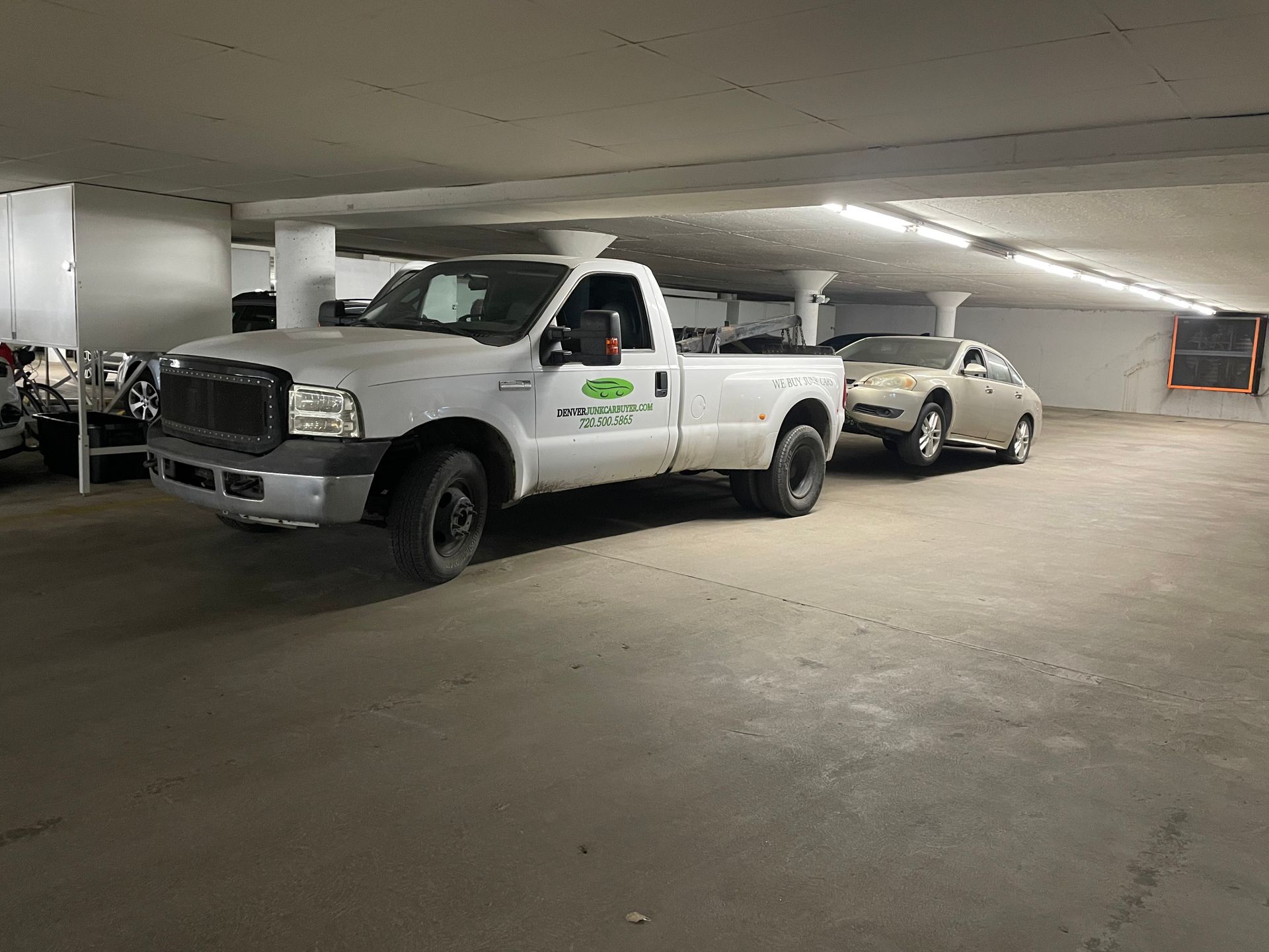 White pickup and silver sedan parked in an underground garage with concrete pillars and ceiling lights