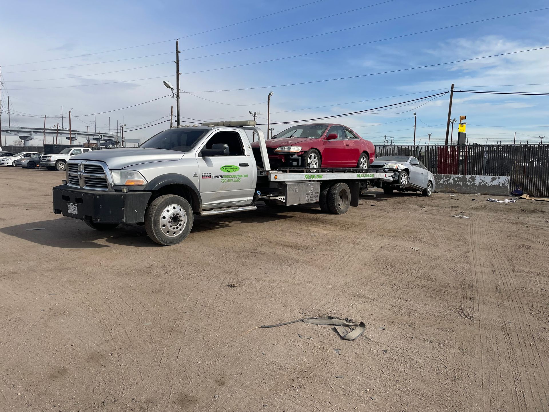 Tow truck carrying a red car in an industrial lot under a blue sky