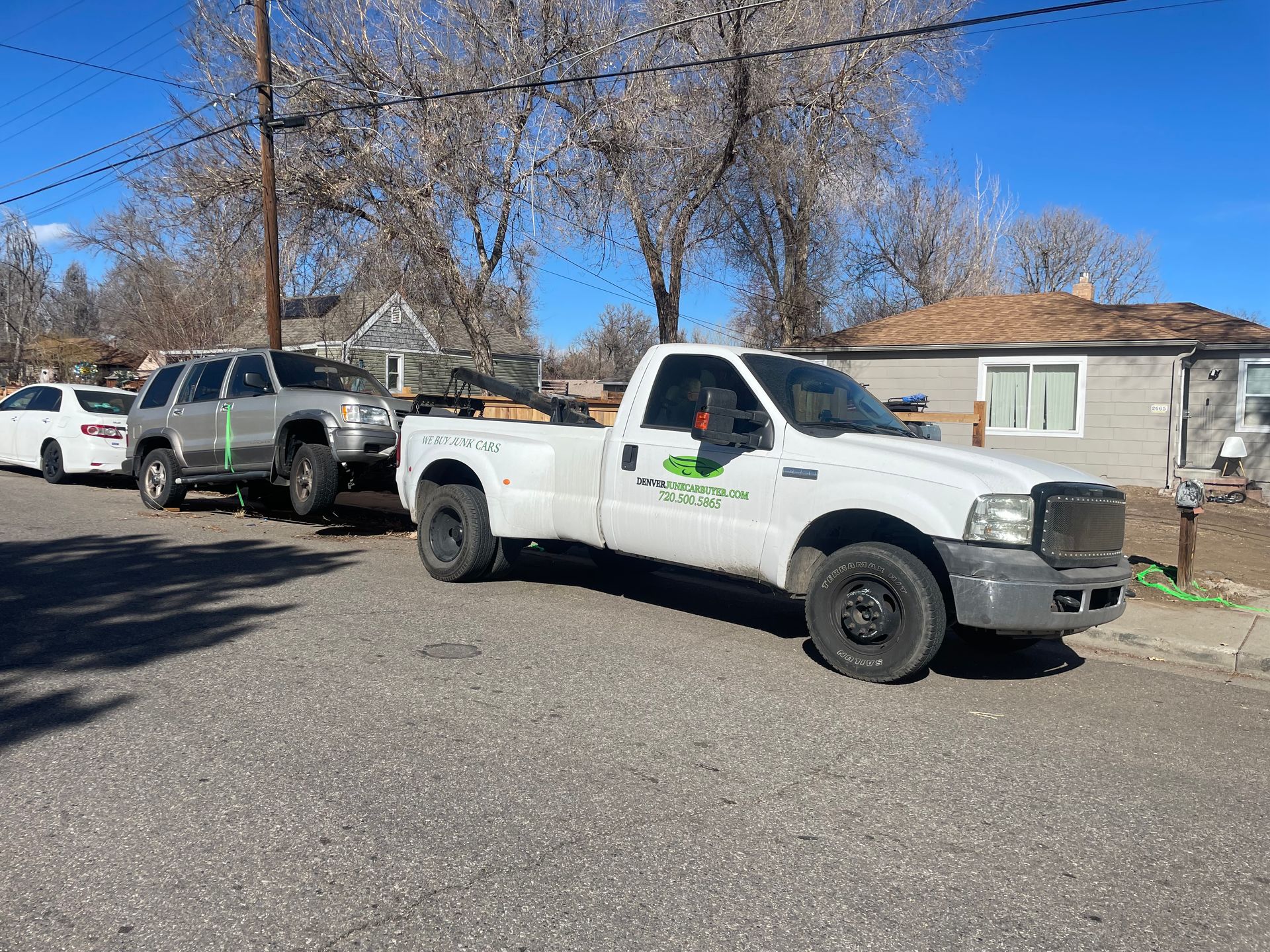 White pickup truck parked on a residential street with two vehicles behind it under a clear blue sky