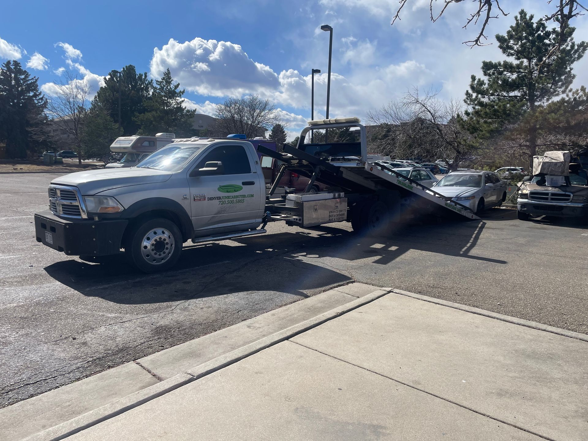 Tow truck loading a silver car onto a flatbed in a parking lot under a partly cloudy sky