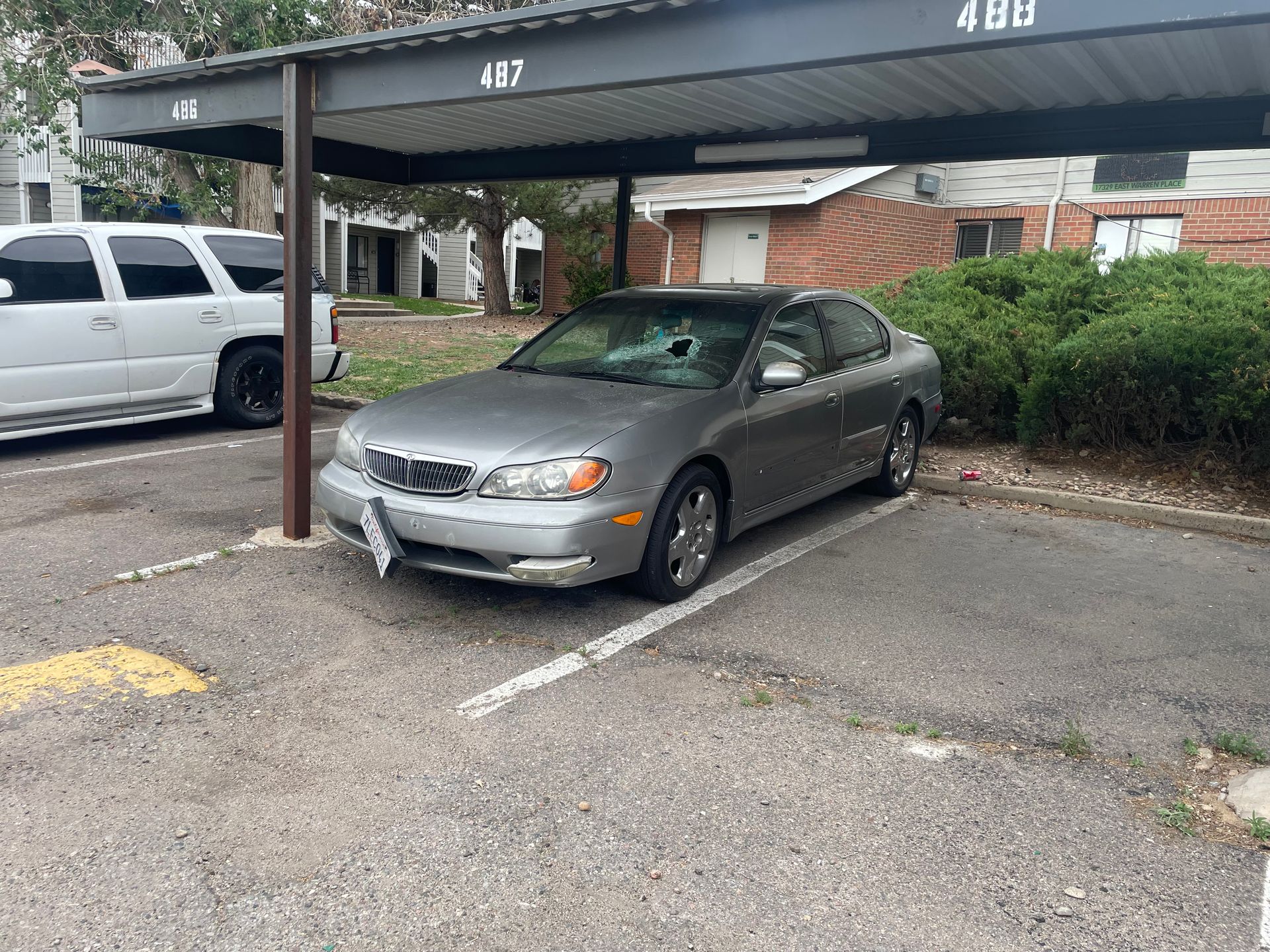 Gray sedan parked under a covered carport in an apartment lot, with a white SUV beside it.