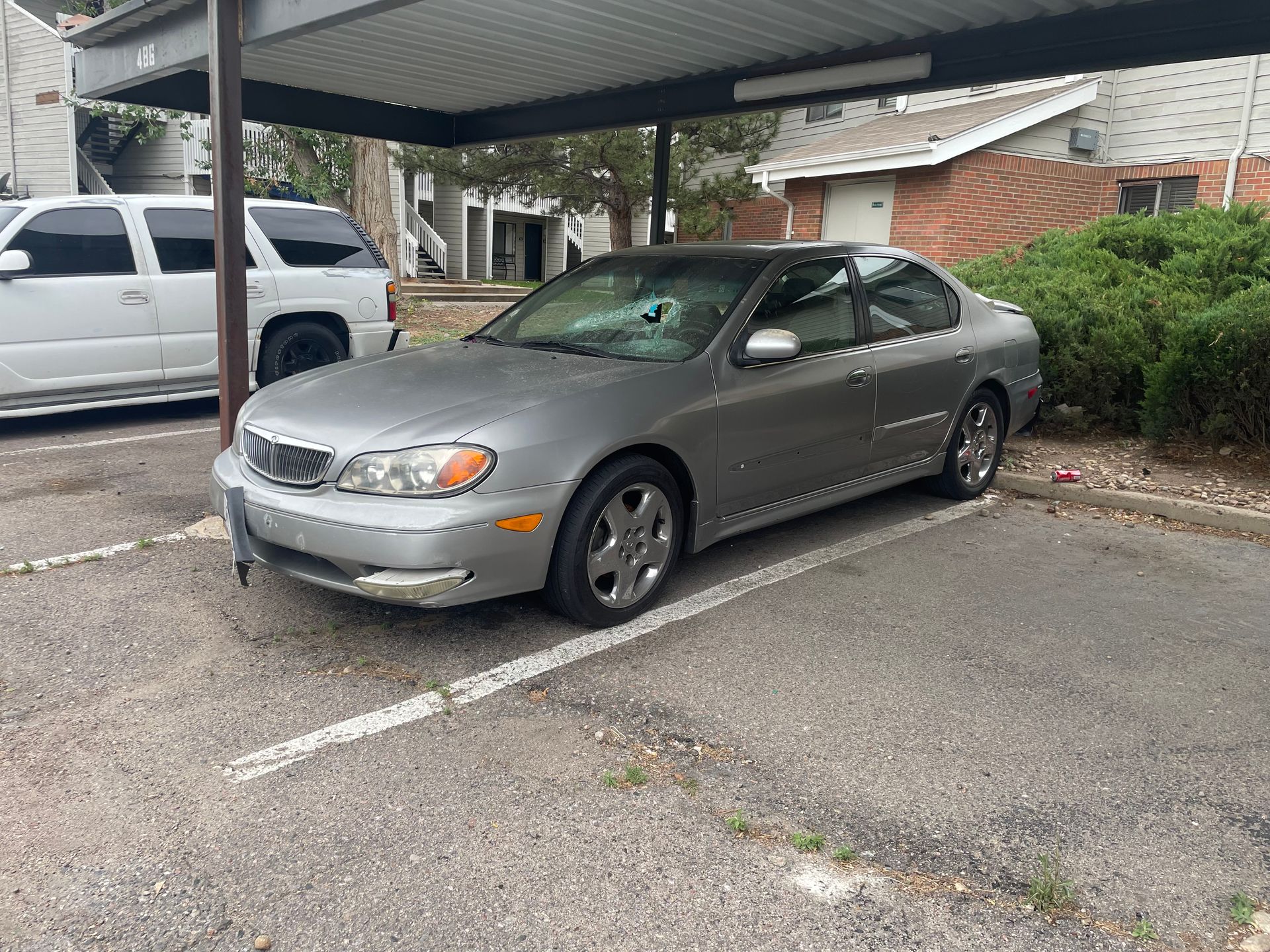 Silver coupe parked under a carport next to a white SUV in an apartment lot.