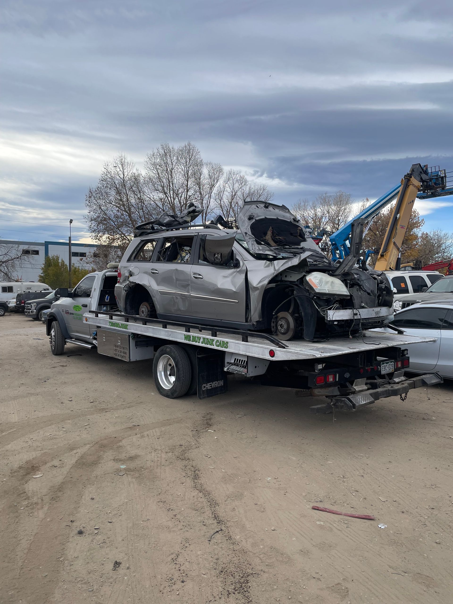 Severely damaged silver SUV on a tow truck in a gravel lot, with heavy debris and overcast sky.