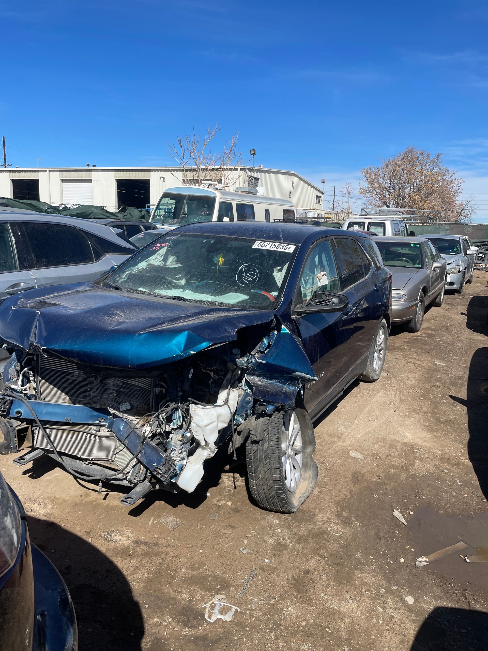 Severely front-damaged dark blue car in a dirt lot among other parked vehicles.