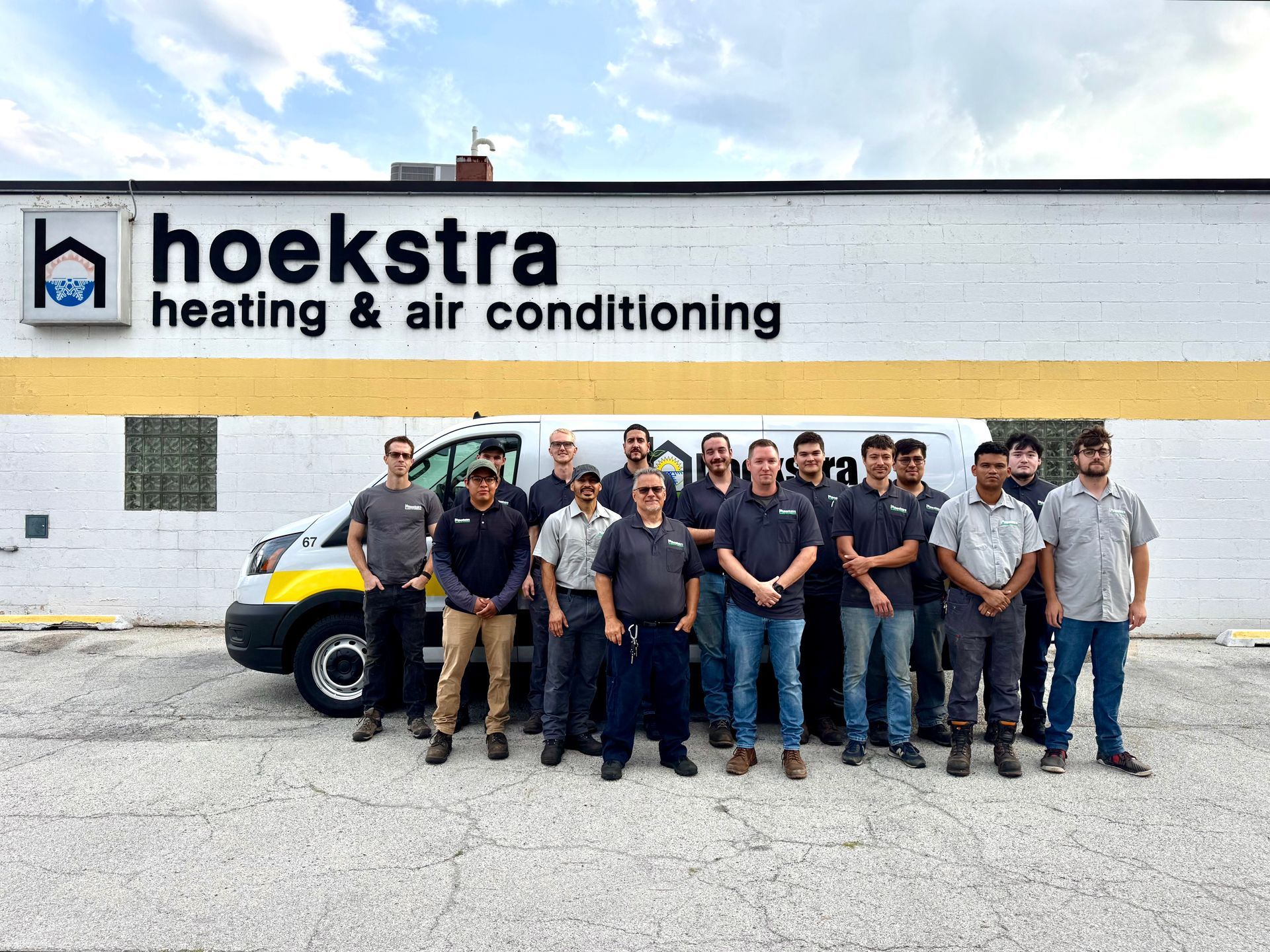 Hoekstra HVAC team stands in front of their building and van. White building, blue sky, sunny day.