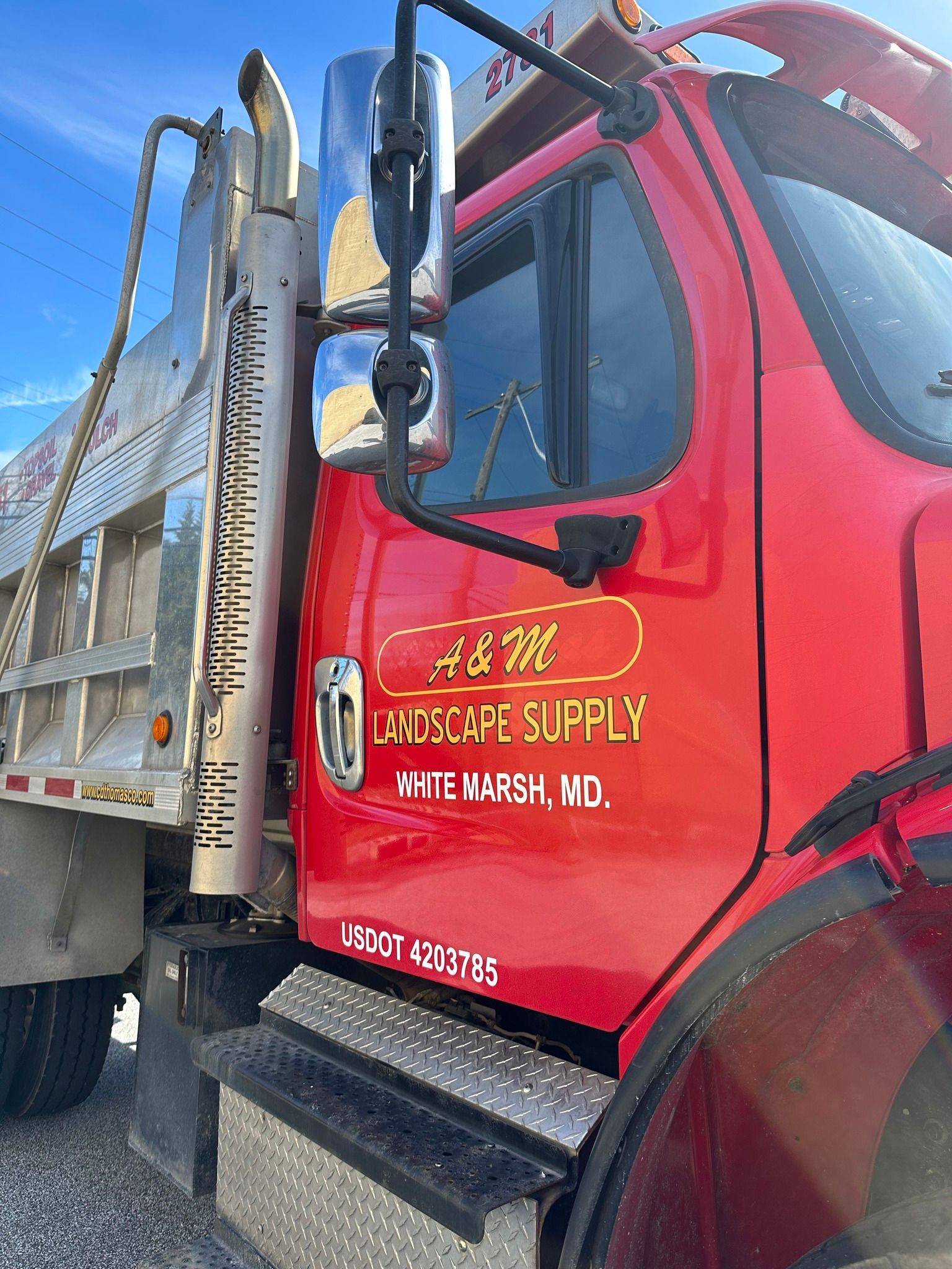 A red dump truck is parked on a gravel road.