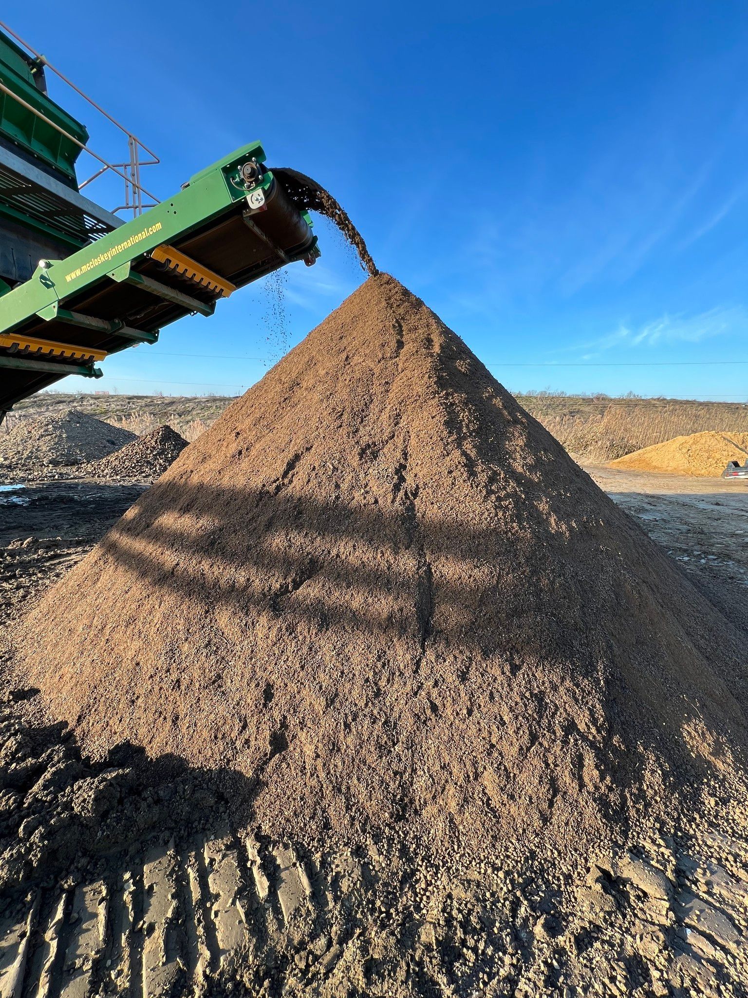 A pile of dirt is being poured from a conveyor belt into a pile.