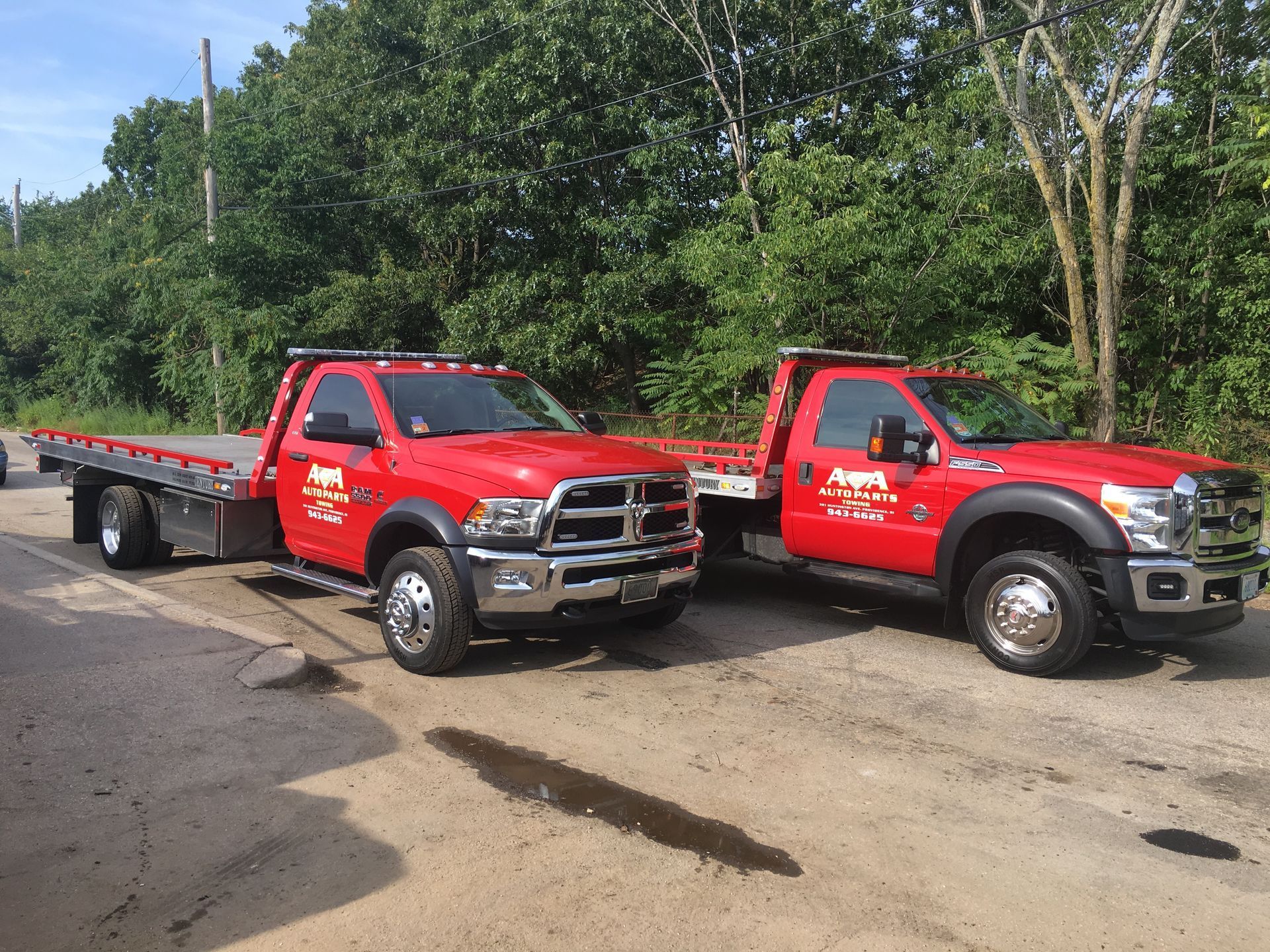 Two red tow trucks are parked next to each other on the side of the road.