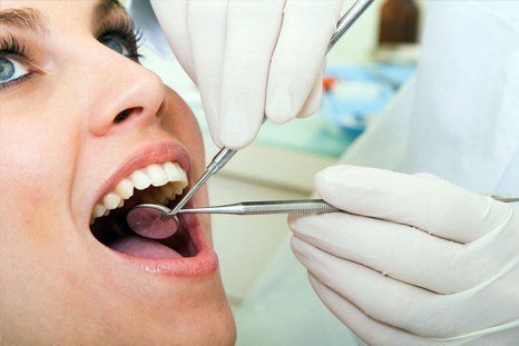 Dentist examining a patient’s open mouth with dental mirror and gloved hands.