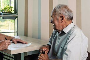 Man seated at a table during a consultation with another person taking notes.