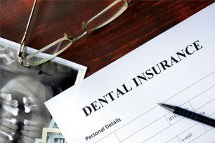 Dental insurance form with eyeglasses, dental x-ray, and pen on a wooden desk.