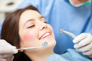 Dental hygienist cleaning a smiling patient’s teeth in a dental office.