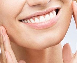 Close-up of a smiling mouth with white teeth and hands framing the face.