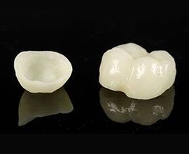 White dental crown beside a matching tooth cap on a black reflective surface.