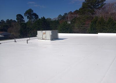 White commercial flat roof with HVAC unit. Trees and blue sky in background.
