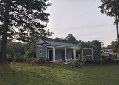 Gray and white shed-like structures with a green roof, set in a grassy yard, with trees in the background.