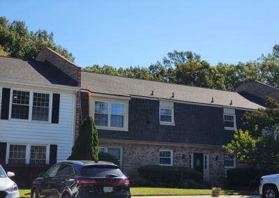 Townhouses with dark shingle roofs, brick and white siding, trees in the background, blue sky.