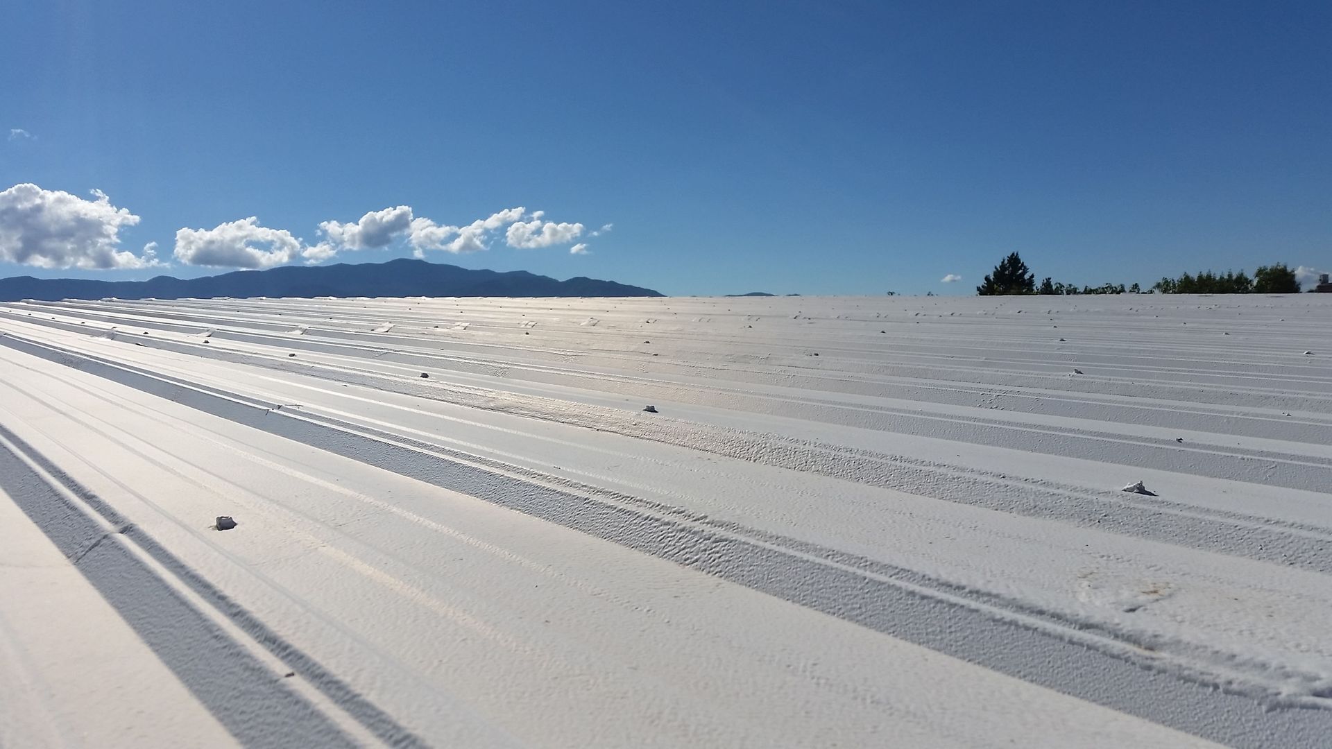 Bright white metal roof under a blue sky, mountains in the distance.
