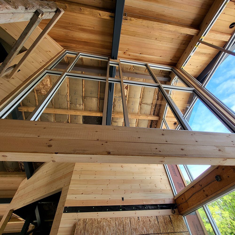 Interior view of a building under construction, featuring large windows and exposed wood beams.