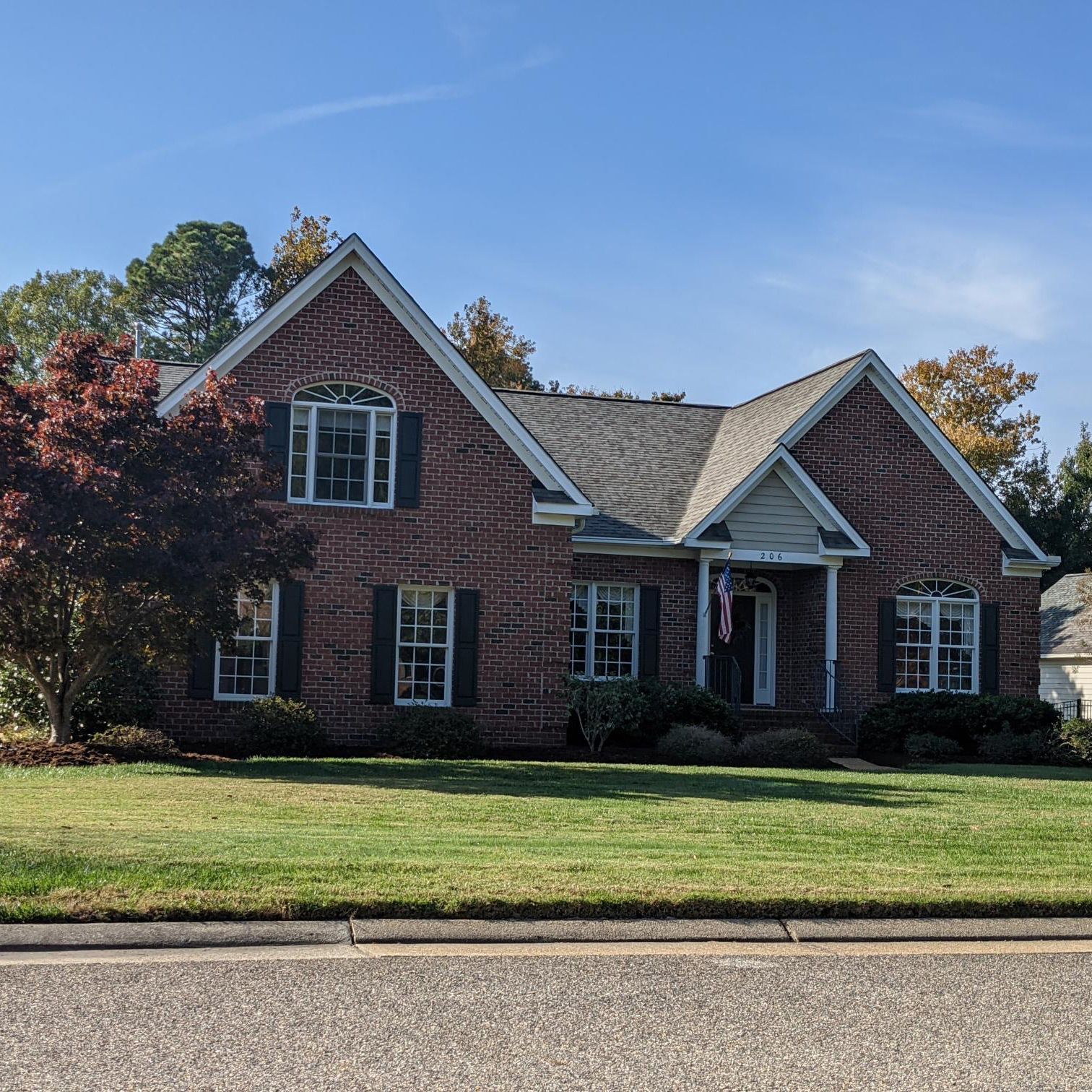 Brick house with green lawn and trees, blue sky in background.