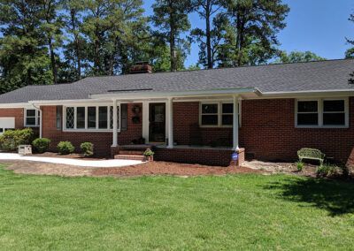 Red brick ranch house with white trim, porch, and green lawn on a sunny day.