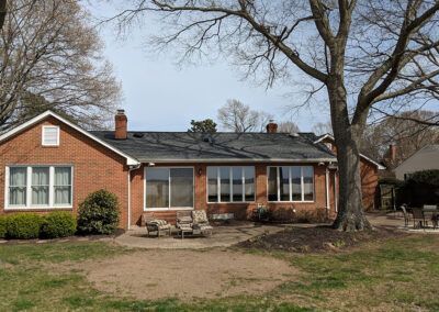 Brick house with black roof, large windows, and a tree in the yard.