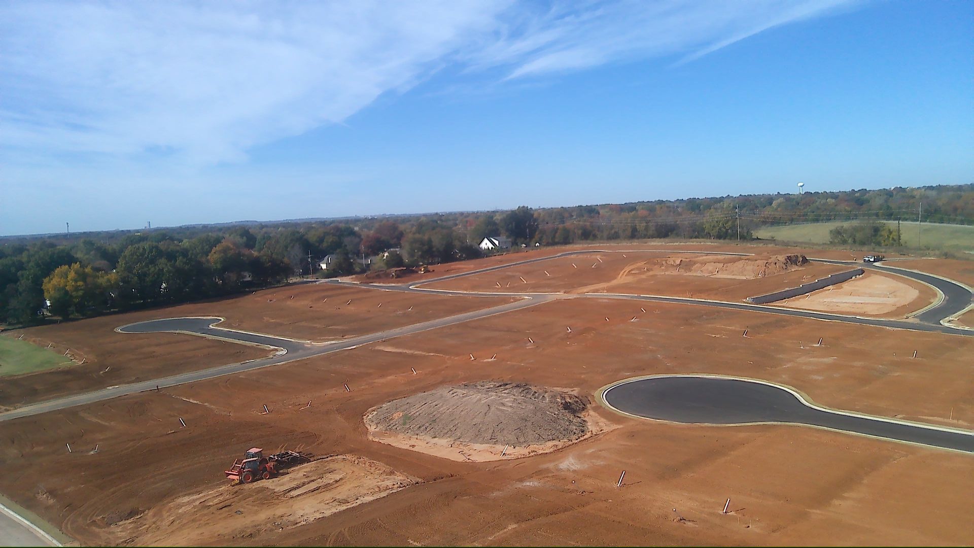 Construction site with roads outlined in black, cleared land, and a blue sky.