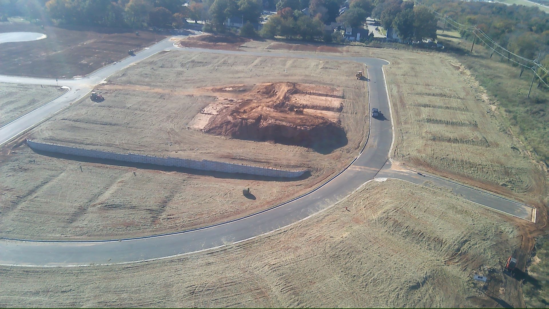 Aerial view of construction site with road and empty lots, brown and gray hues.