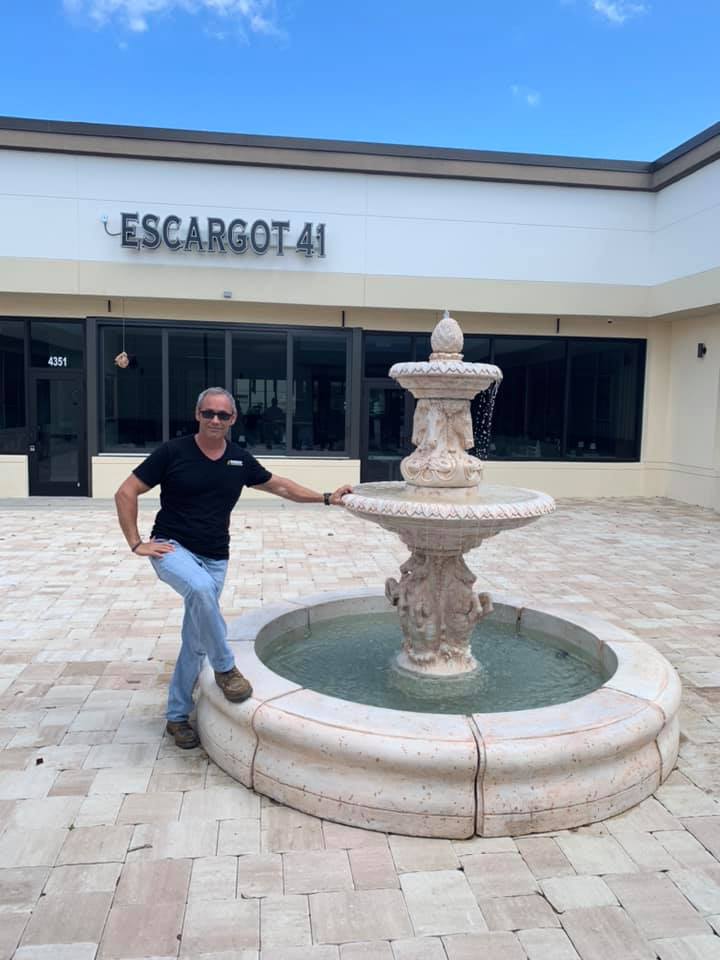 A man is standing next to a fountain in front of a building.