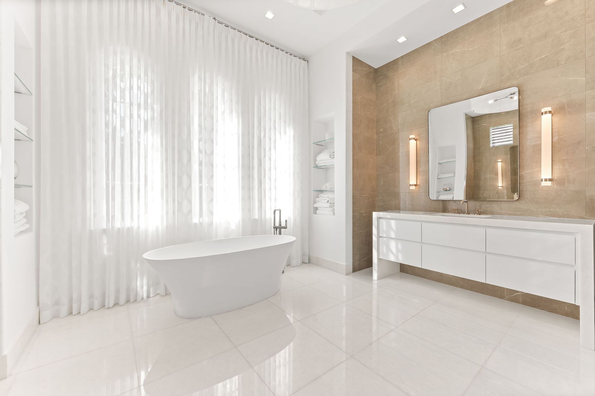 Modern white bathroom with freestanding tub, vanity, and large window with sheer curtains.