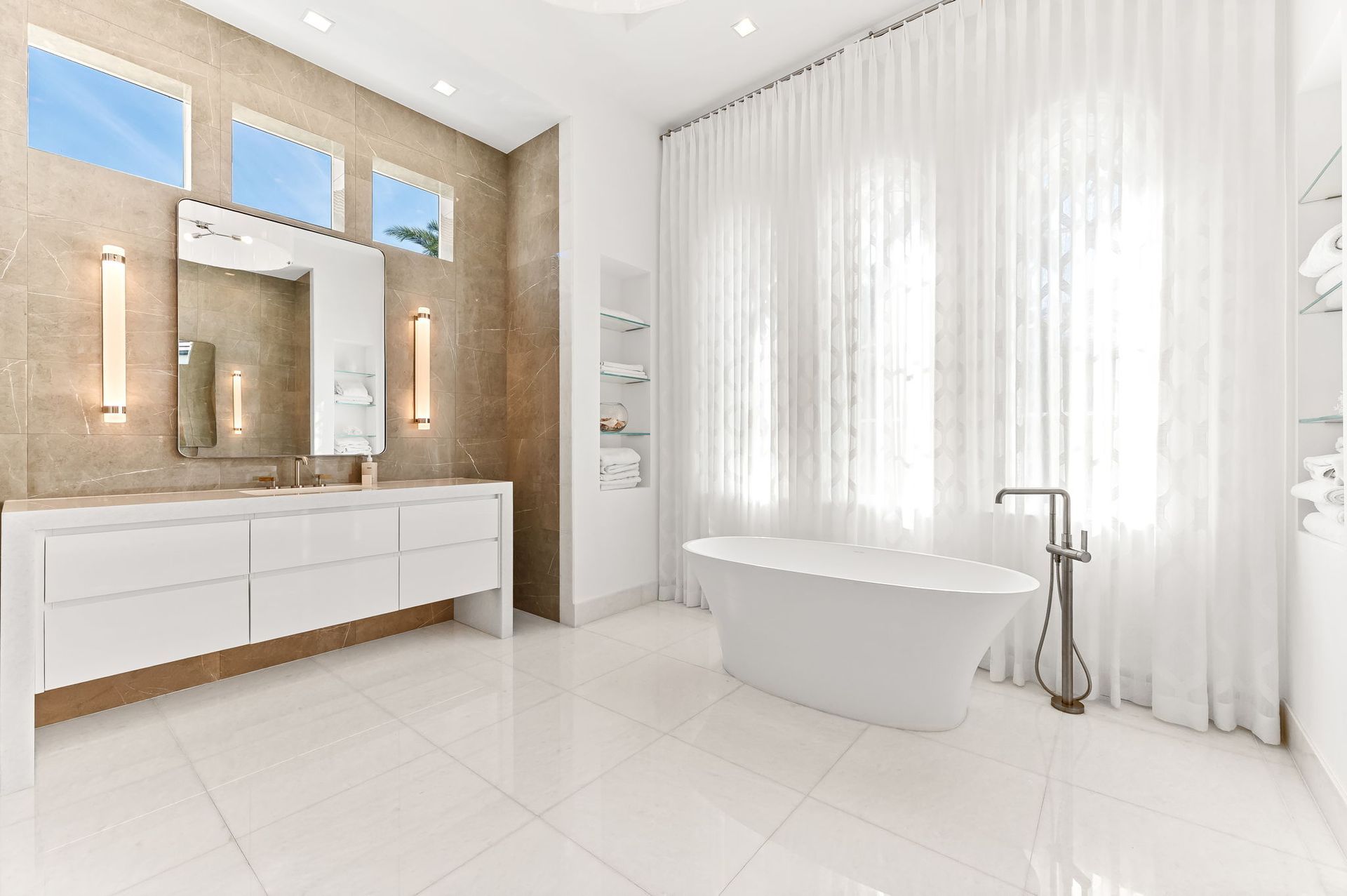 Bright white bathroom with freestanding tub and vanity with long mirror. Beige accent wall.