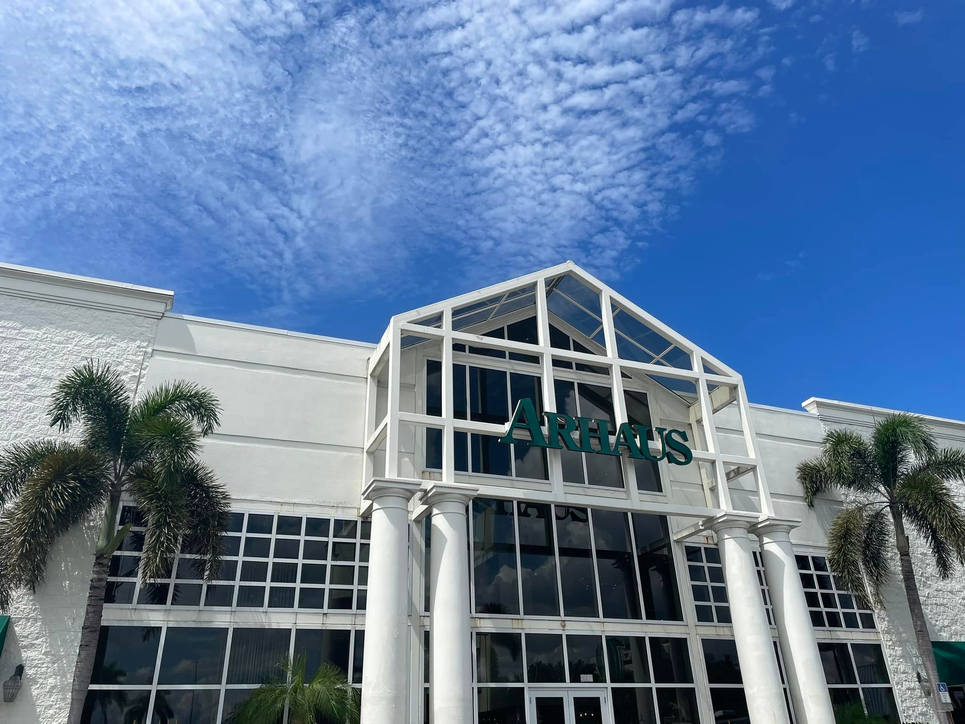 A large white building with columns and palm trees in front of it.