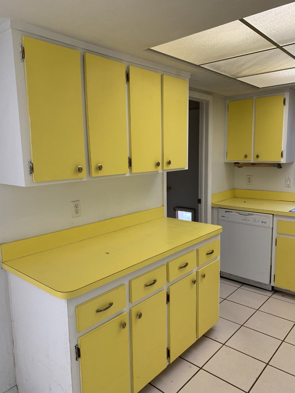 A kitchen with yellow cabinets and white counter tops
