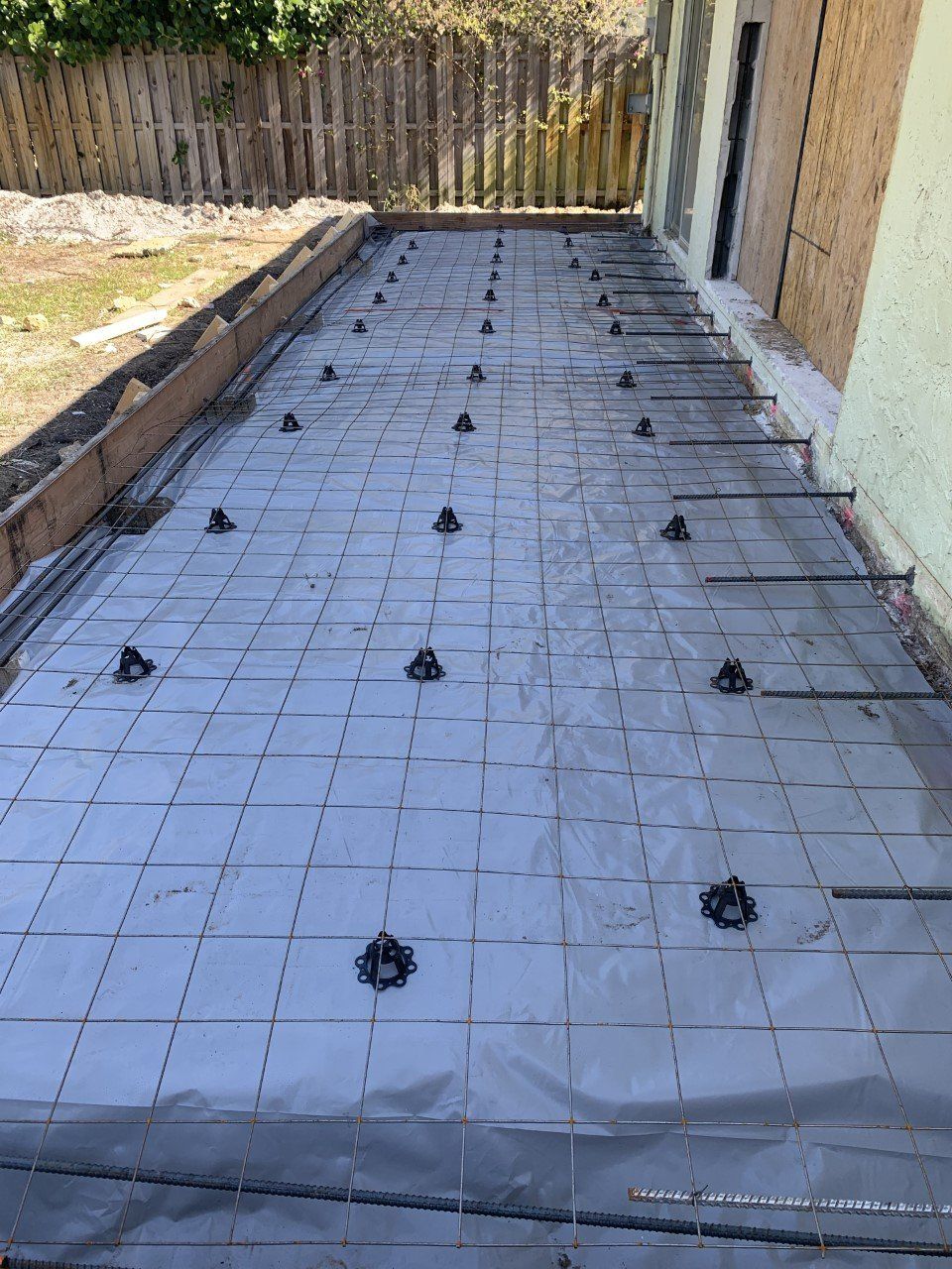 A concrete floor is being built in a backyard with a fence in the background.