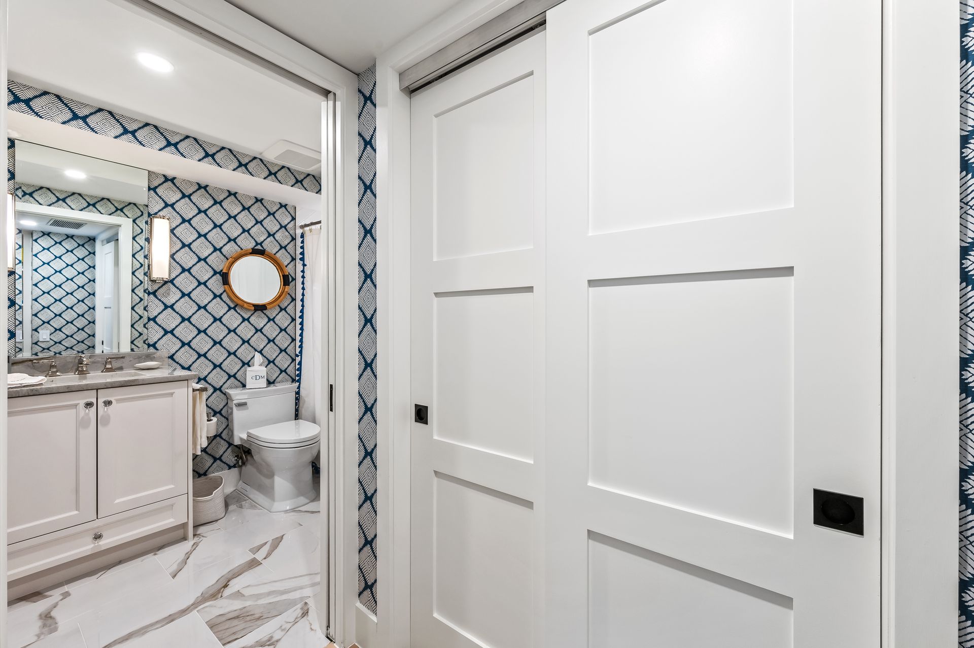 A bathroom with a toilet , sink , mirror and sliding doors.