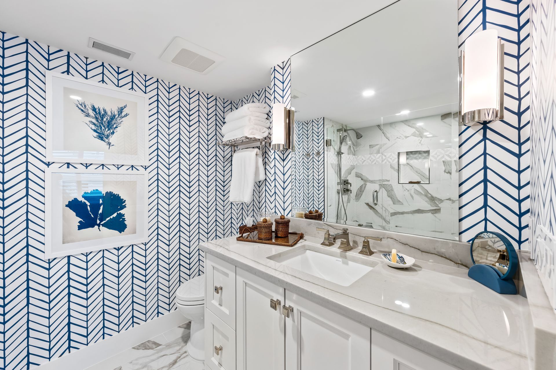 A bathroom with a sink , toilet , mirror and blue and white wallpaper.