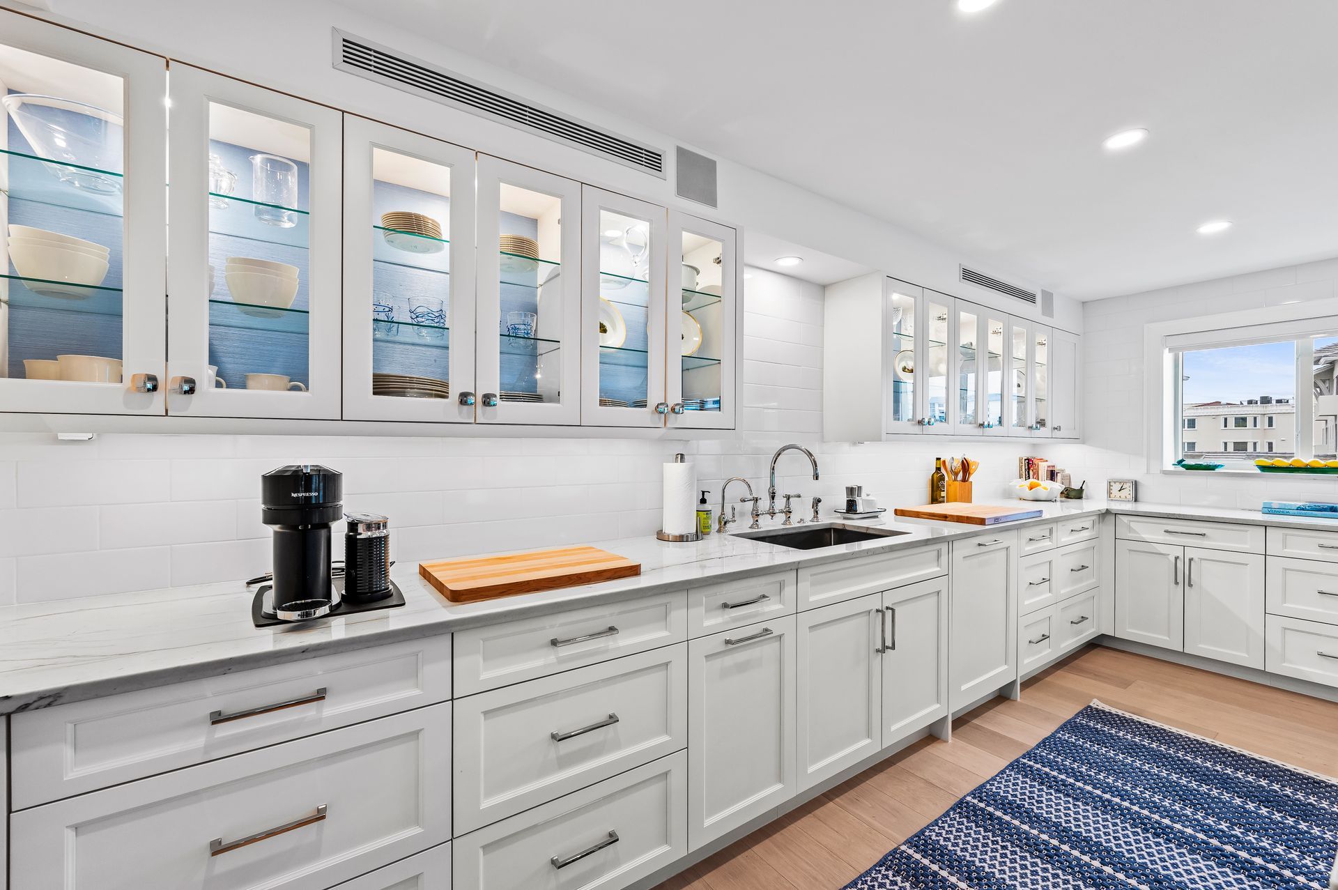 A kitchen with white cabinets , a sink , and a blue rug.