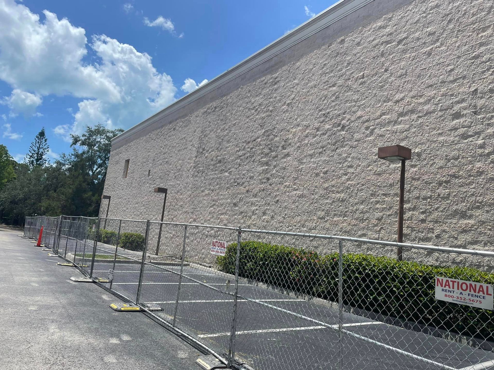 A chain link fence surrounds a parking lot in front of a large brick building.