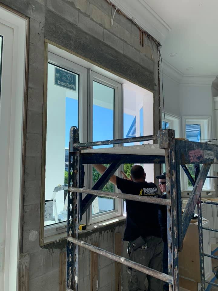 A man is standing on a scaffolding in front of a window.