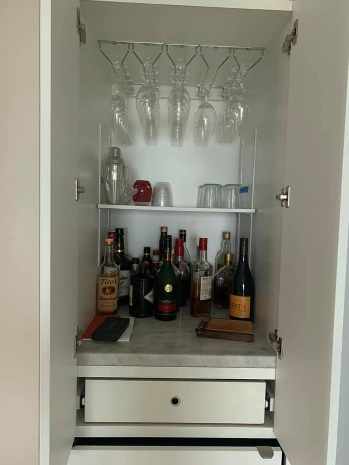 A cabinet filled with bottles , glasses , and a drawer.