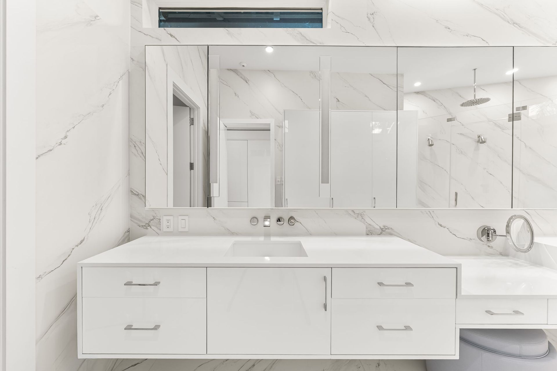 White marble bathroom with floating vanity and large mirrors.