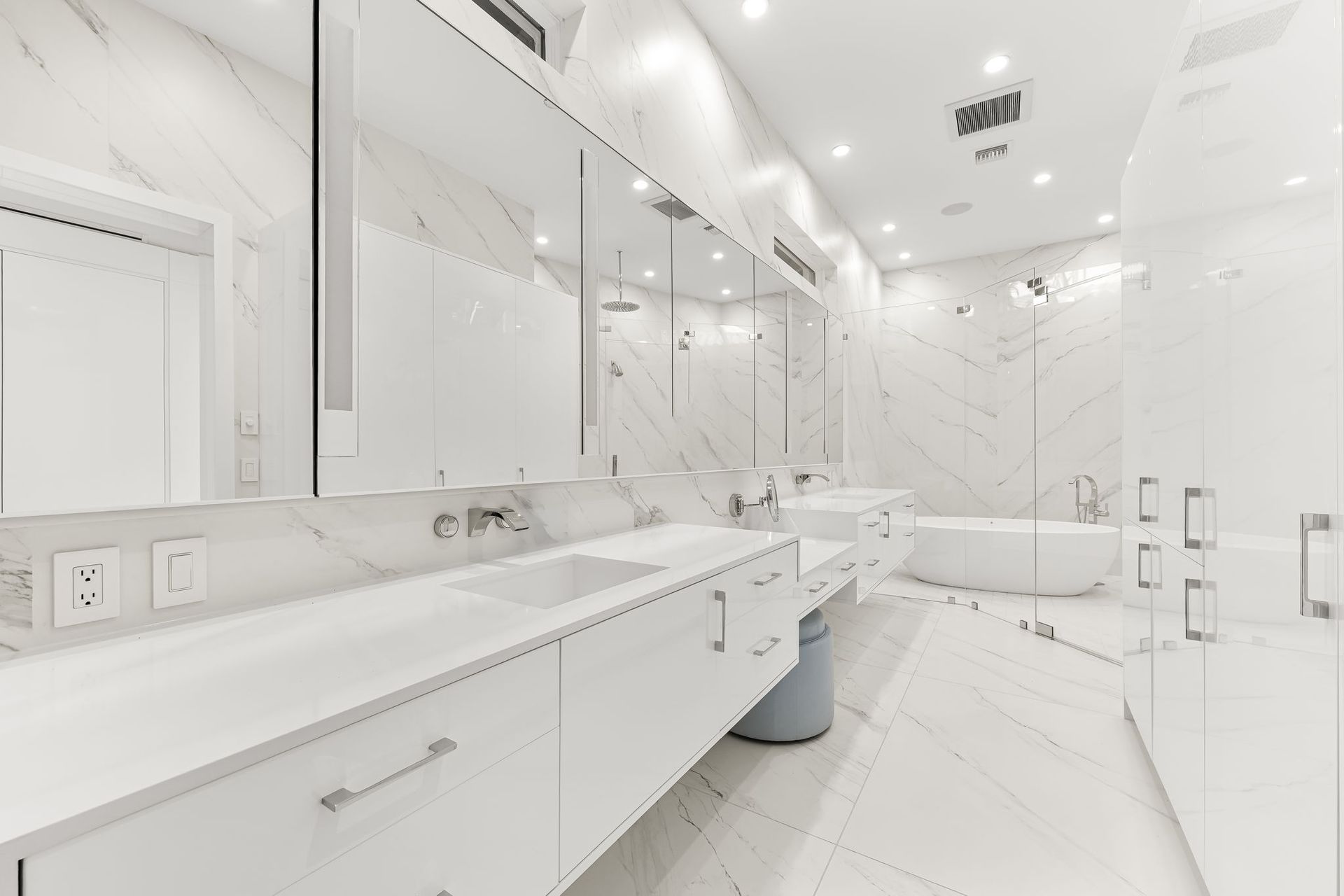 White, modern bathroom with marble walls and countertops, double sinks, and a bathtub.